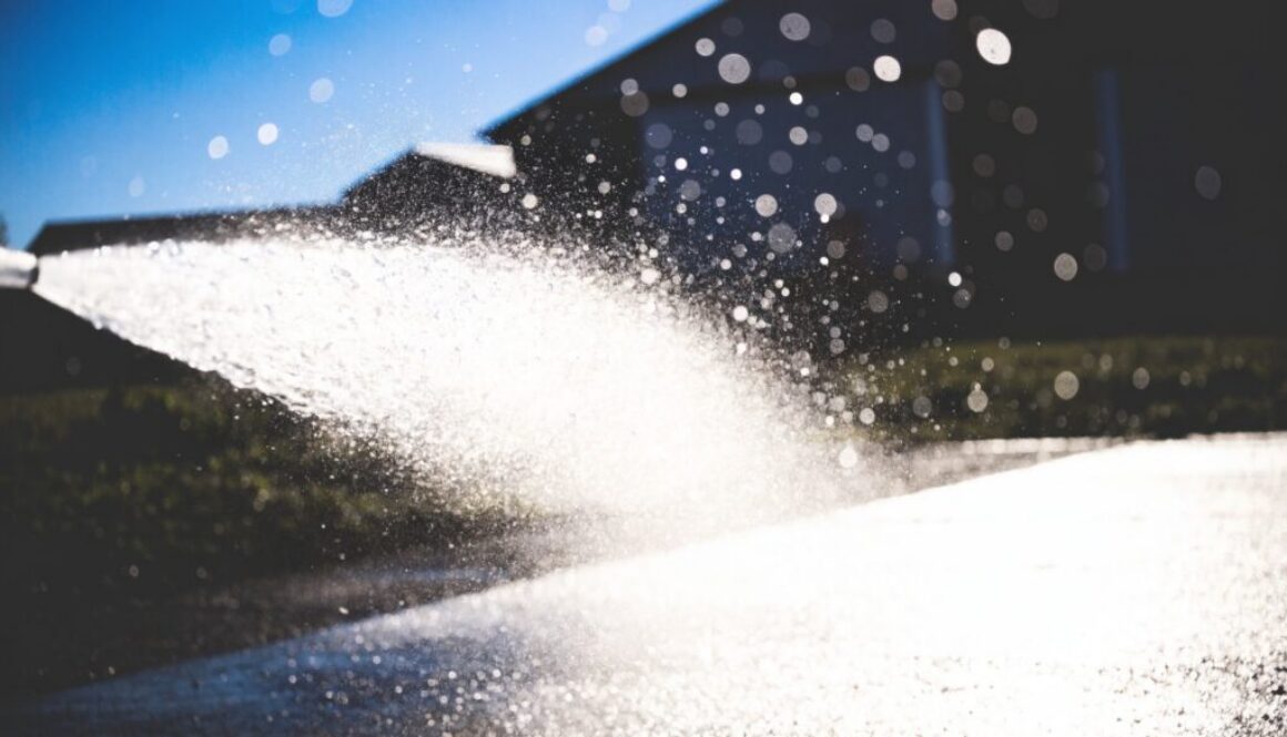 Kräftiger Wasserstrahl mit Sprühnebel beim Reinigen eines Hofbodens